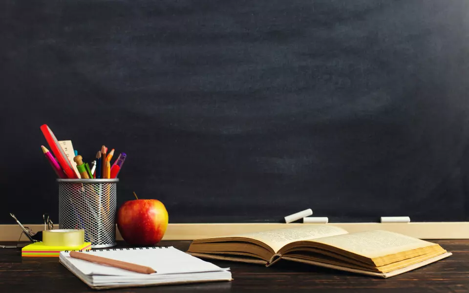 Foto com uma maça, um livro aberto e materiais escolares